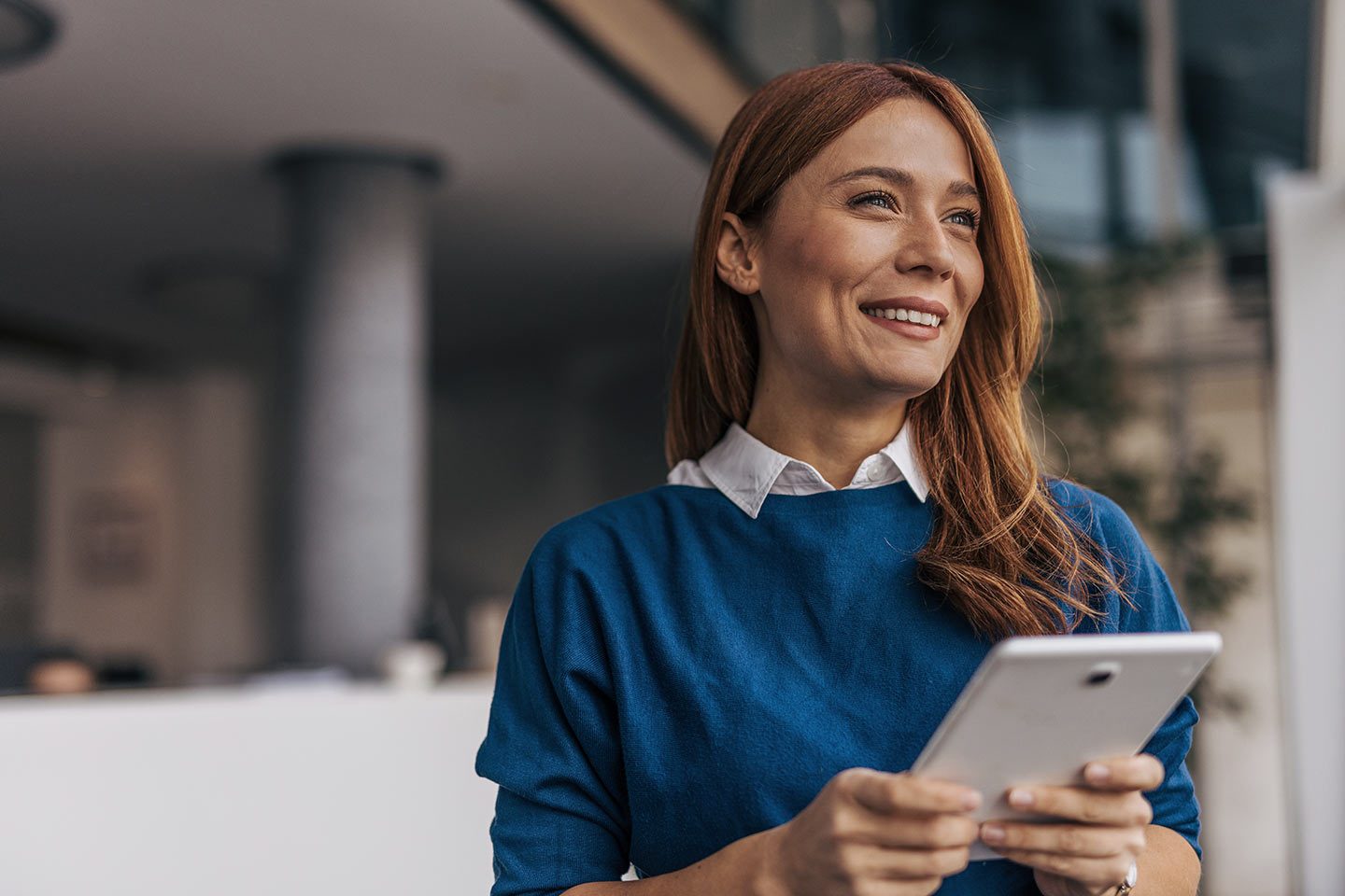 Assistant with red hair smiling and holding a tablet in her hands